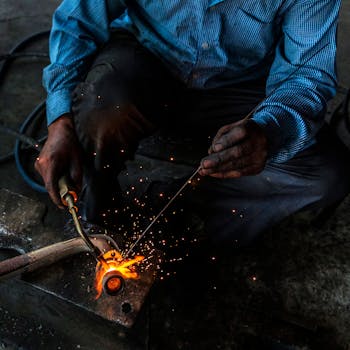 From above of crop unrecognizable workman using welding machine with gas flame while working with metal pipe