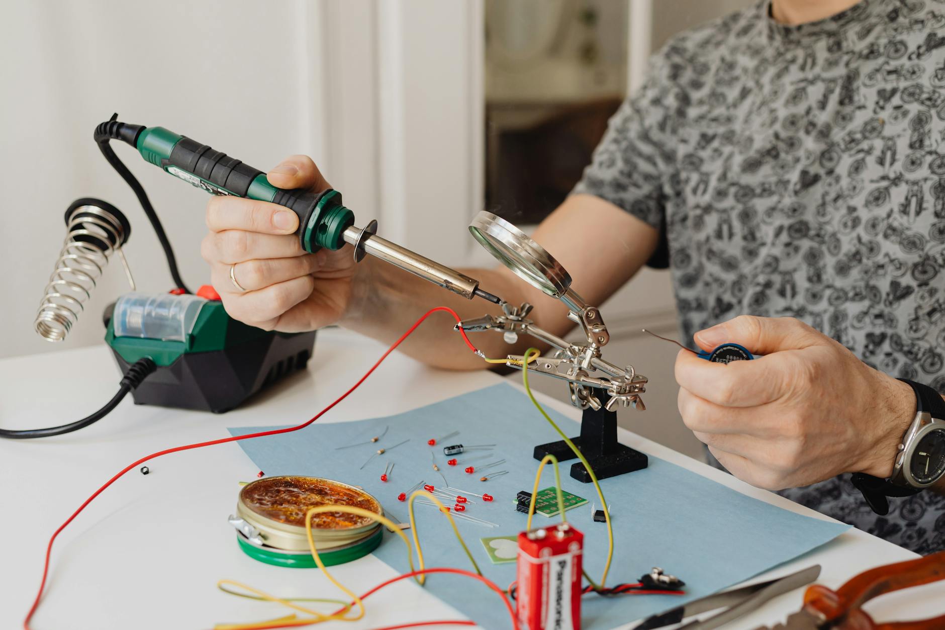 Technician using a soldering iron and magnifying glass to fix electronic circuit components indoors.