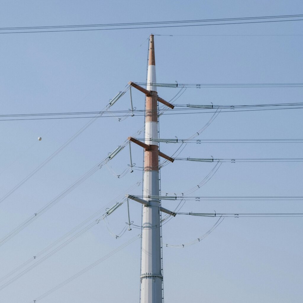 A towering high voltage power line structure set against a clear blue sky, representing energy infrastructure.